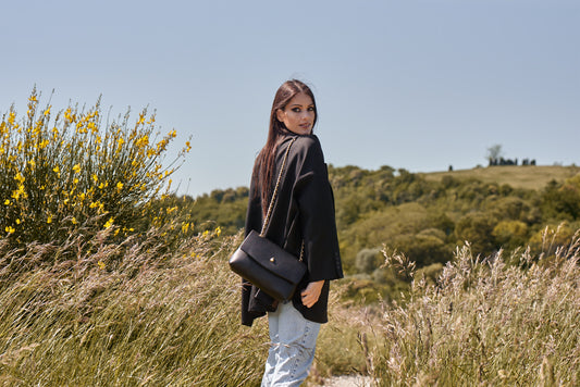 Woman wearing black leather shoulder bag with gold chain outdoors back view