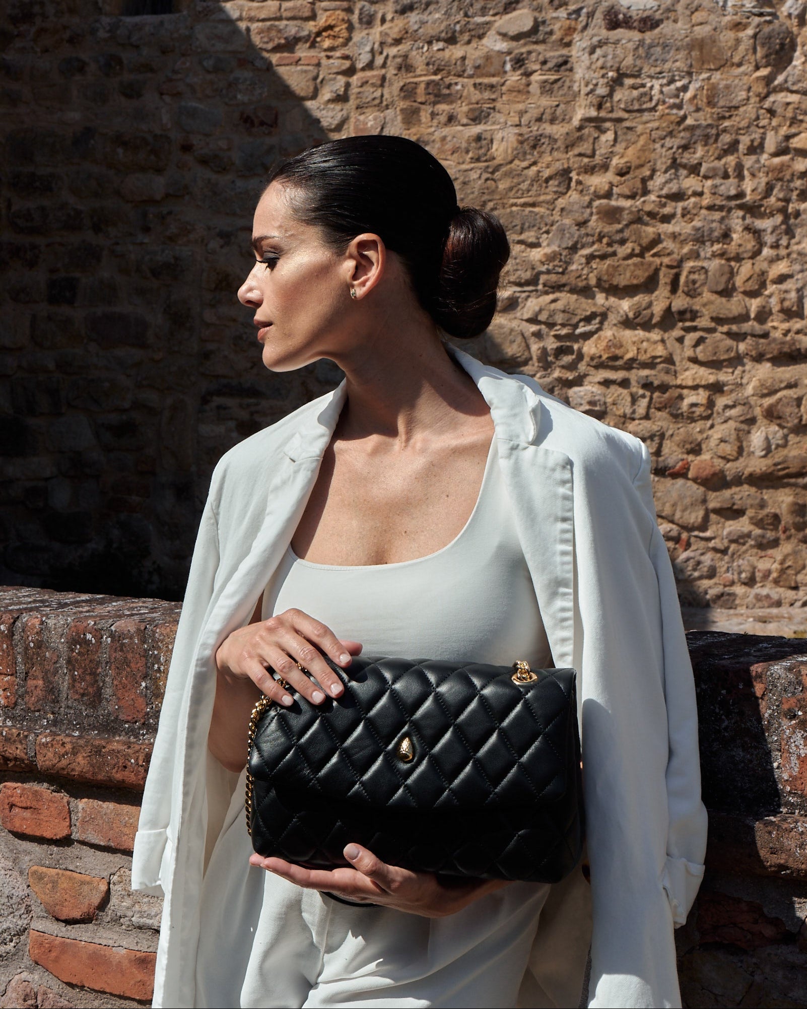 Elegant woman holding Archiduchesse black quilted leather bag by hand in a luxury outdoor setting