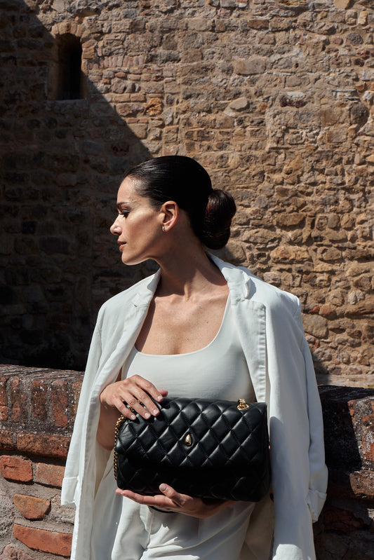 Elegant woman holding Archiduchesse black quilted leather bag by hand in a luxury outdoor setting