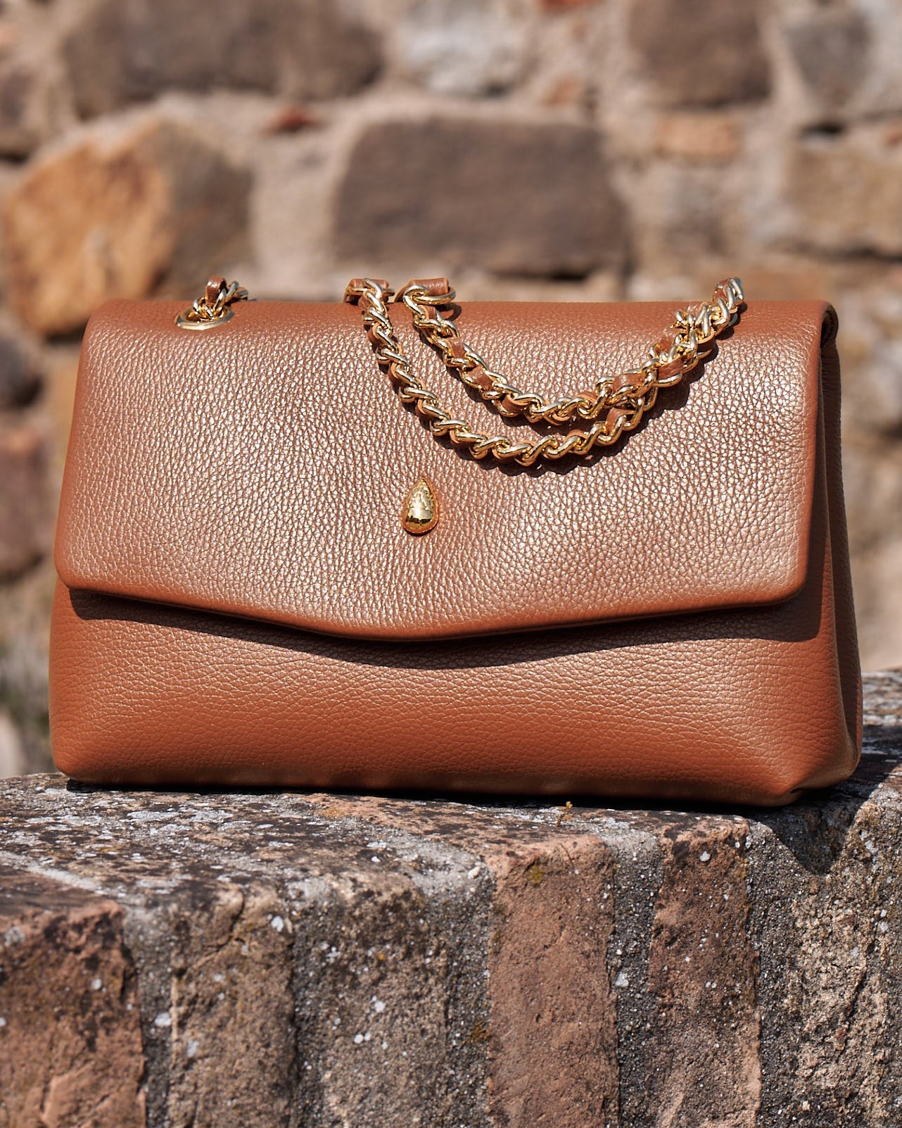 Brown leather bag placed on a stone wall showing texture and shape
