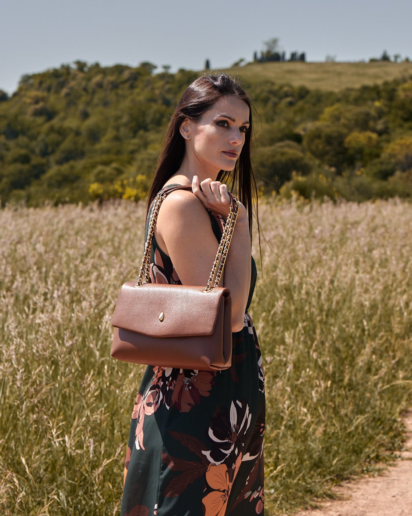 Woman wearing a brown leather shoulder bag in an elegant outdoor setting