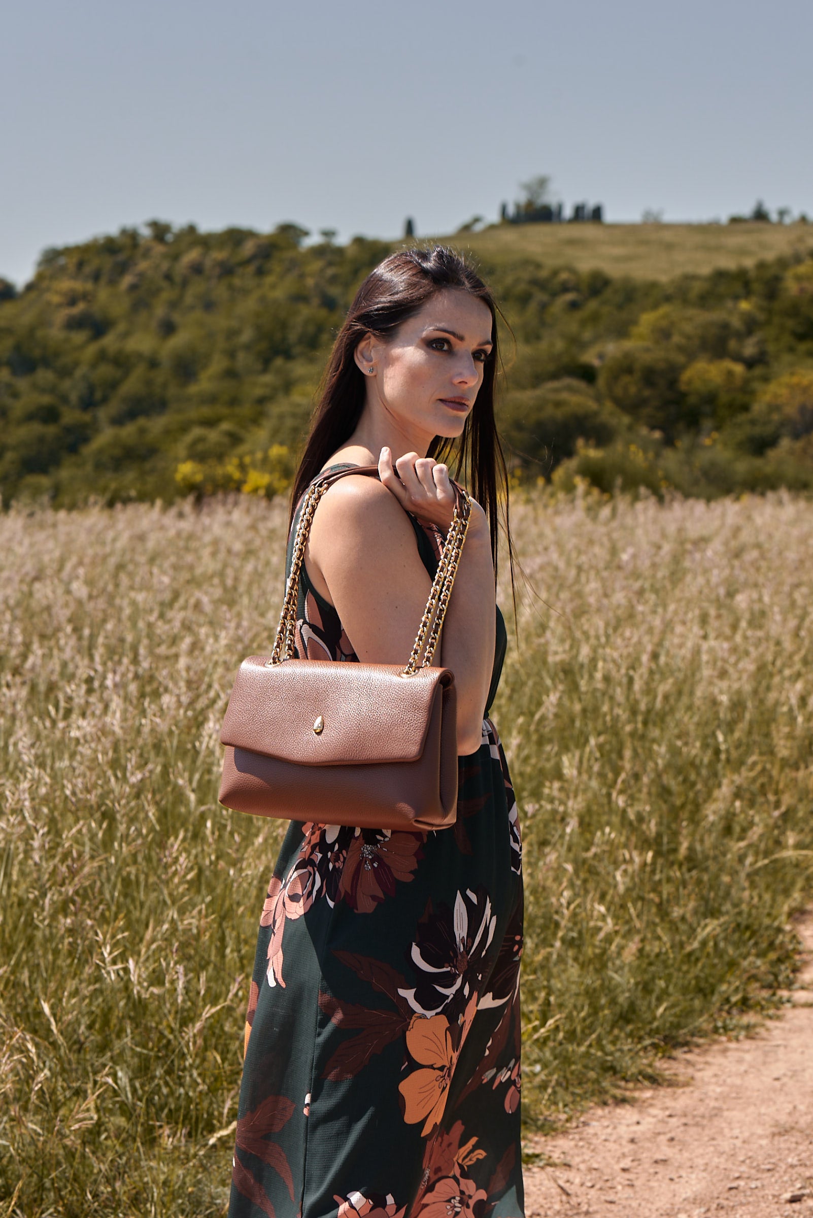 Woman wearing a brown leather shoulder bag in an elegant outdoor setting